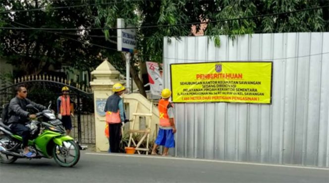 
					Pekerja tengah memasang spanduk terkait pembangunan kantor Kecamatan Sawangan.