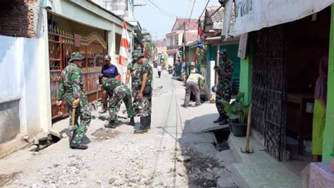 
					Sejumlah anggota TNI dibantu warga sedang memperkeras Jalan Swadaya yang mengalami kerusakan. 