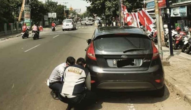 
					Petugas sedang menggembok kendaraan parkir sembarangan di Jalan Nusantara.
