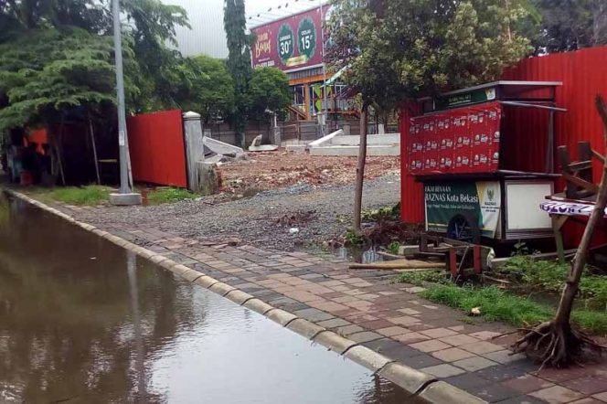 
					Saluran yang ada di depan pintu masuk area pembangunan tertutup tanah serta batu. Akibatnya, air yang ada di saluran tidak dapat mengalir.