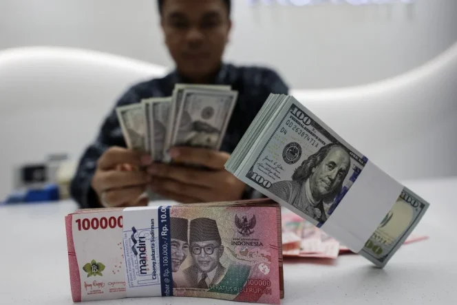 
					Karyawan menghitung uang rupiah dan dolar AS di Jakarta, Selasa (22/7/2025). 